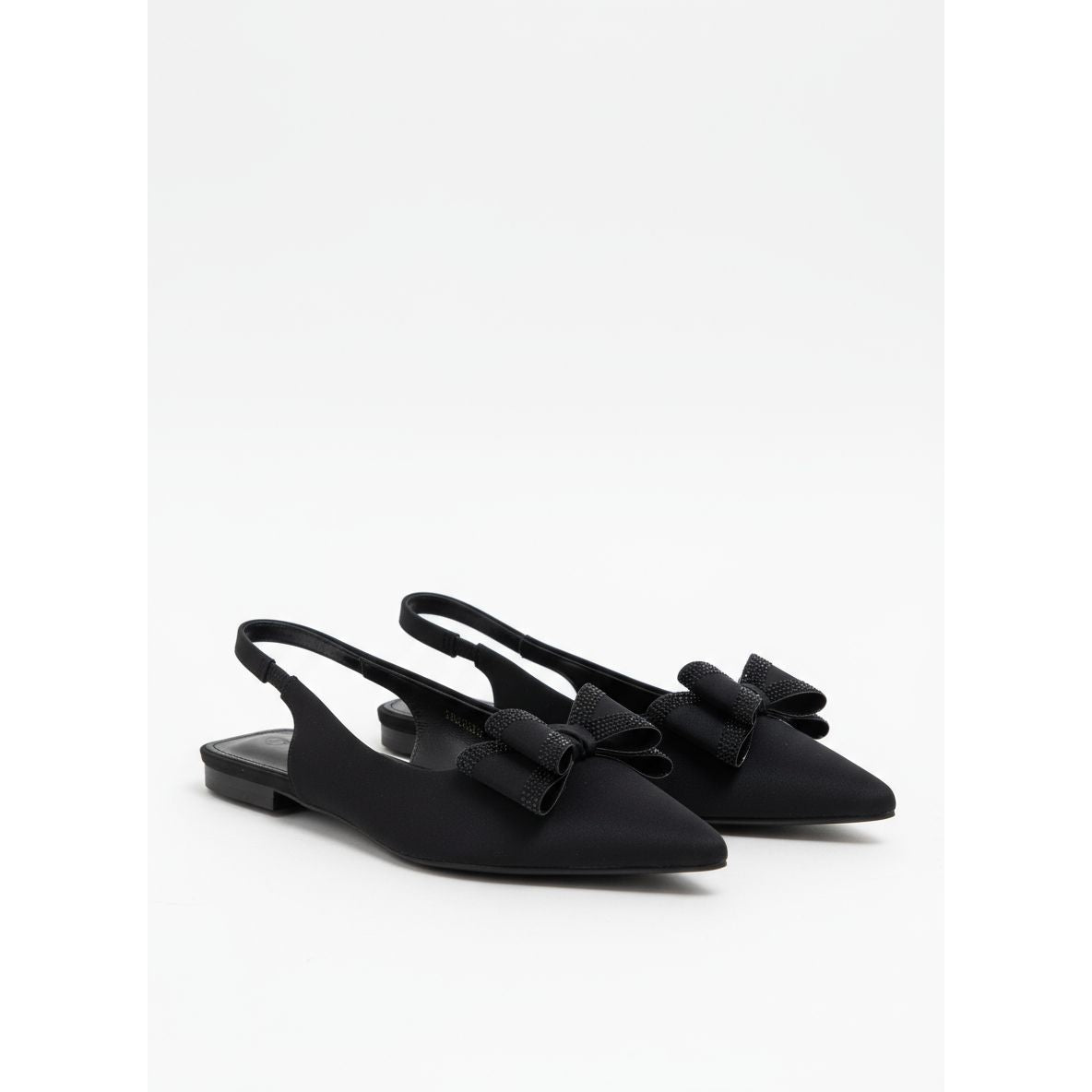 Black high-heeled shoes with bow details on a white surface against a yellow wall.