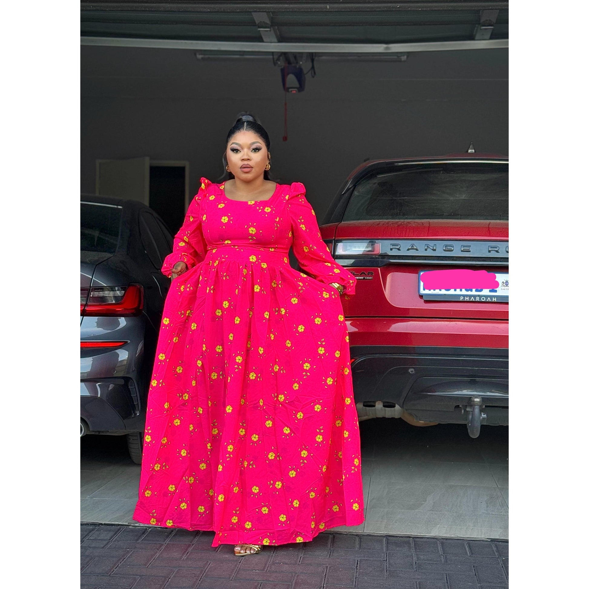 A person wearing a red floral textured dress with a square neckline and flare waist, standing in front of a car.