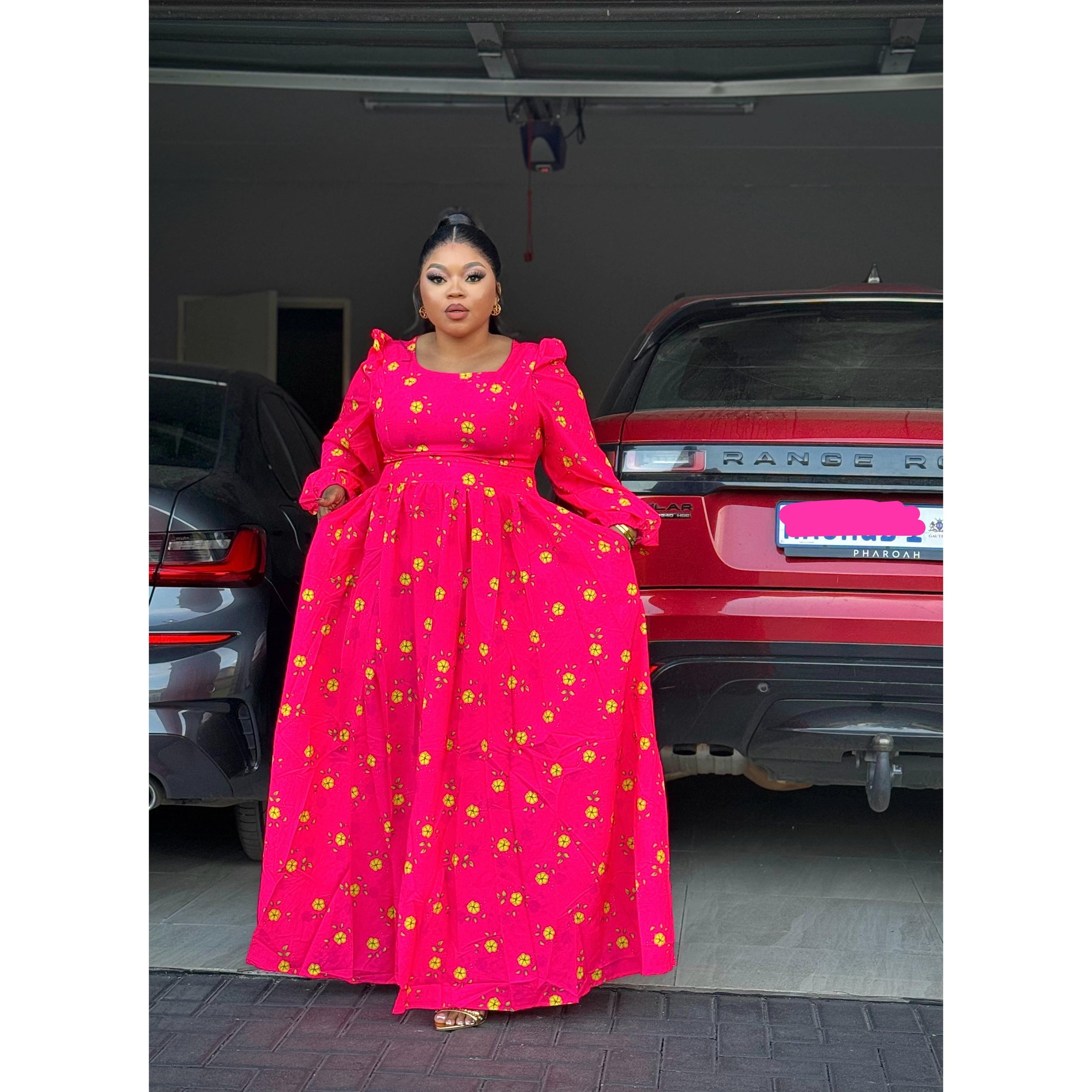 A person wearing a red floral textured dress with a square neckline and flare waist, standing in front of a car.