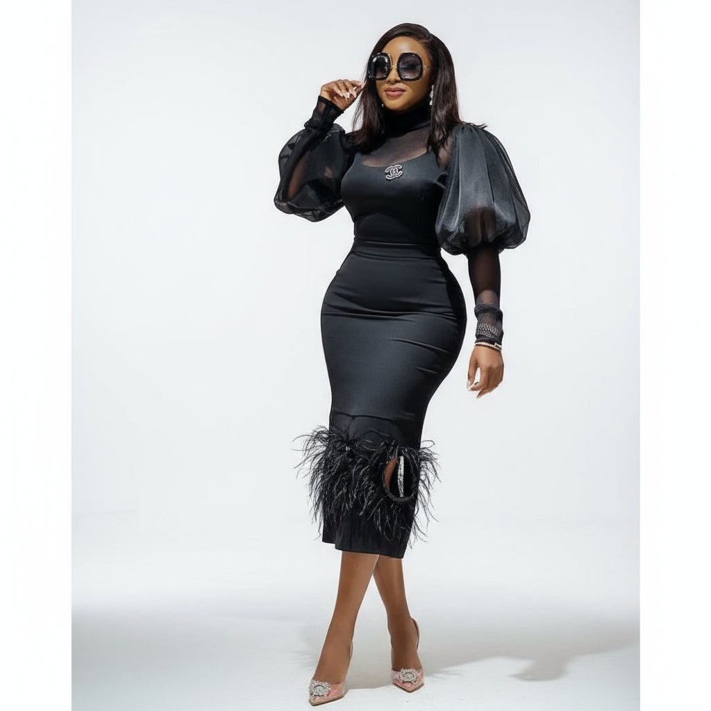 A woman wearing a black dress with puff sleeves and feather patchwork designs standing in a room with a leather sofa.