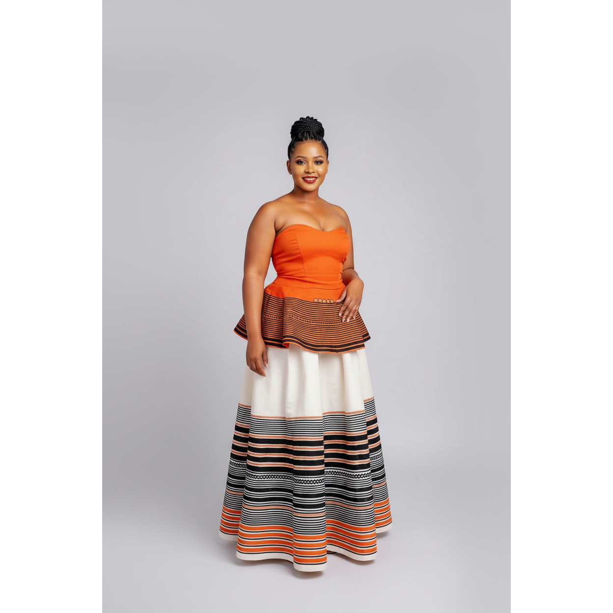 Woman wearing an orange top and a long, patterned skirt on a gray background