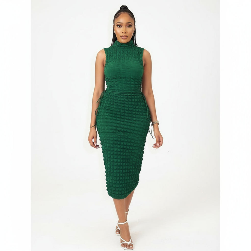 A person wearing a sleeveless turtleneck bodycon dress in green, standing in a room with modern decor.