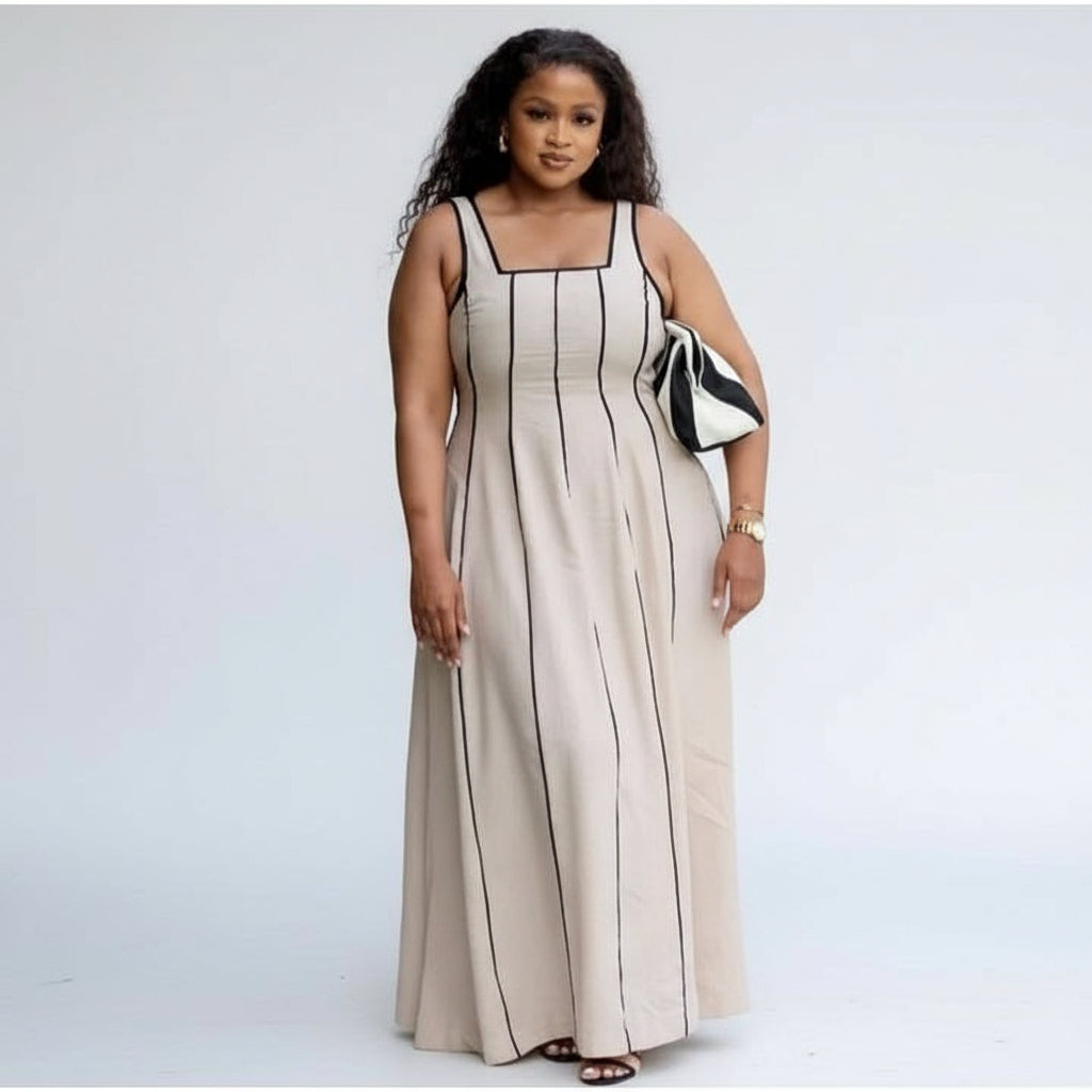 A woman wearing a sleeveless beige midi dress with black striped contrast binding, standing near green plants.