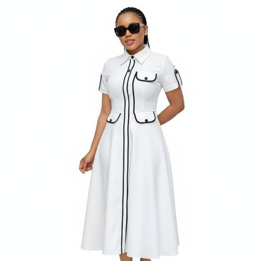 Woman wearing a white dress with black accents standing in front of a glass door.