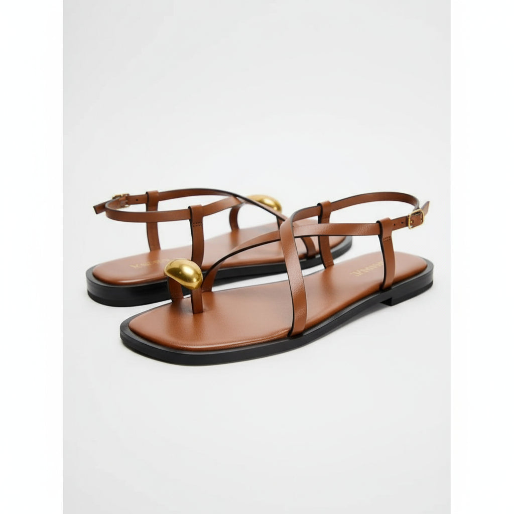 Brown sandal with a gold toe ring on a white background