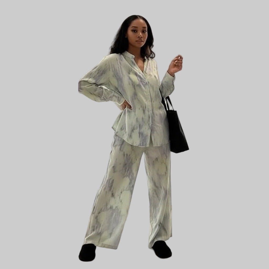 Woman wearing a light-colored outfit with a black handbag on a plain background