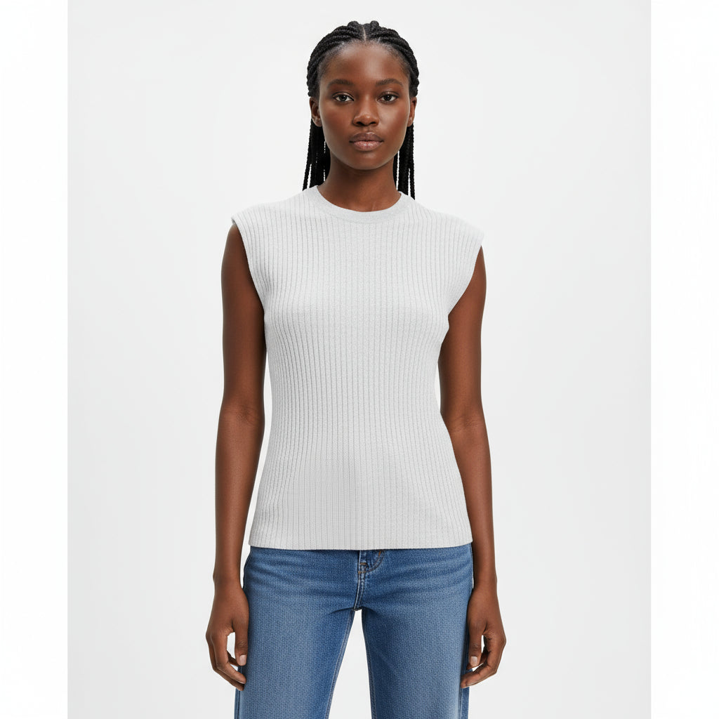 Woman wearing a white ribbed top and blue jeans sitting on a wooden chair.