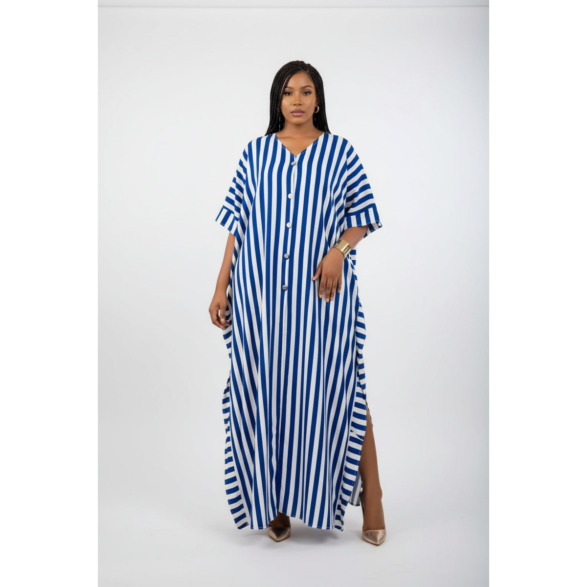 A woman modeling a blue and white vertically striped button-down maxi dress with short wide sleeves and a high side slit, standing against a plain light gray studio background.