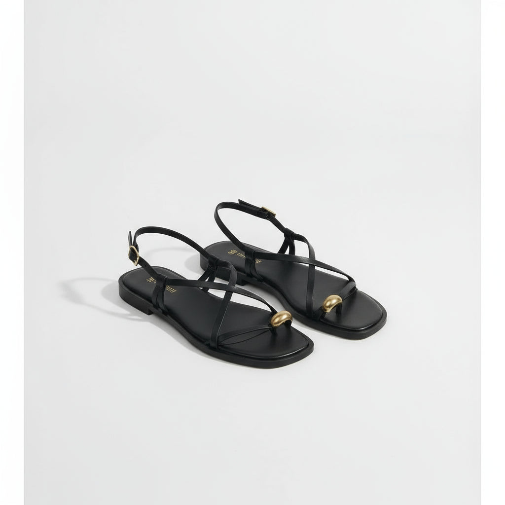 Black strappy sandals worn on a textured surface