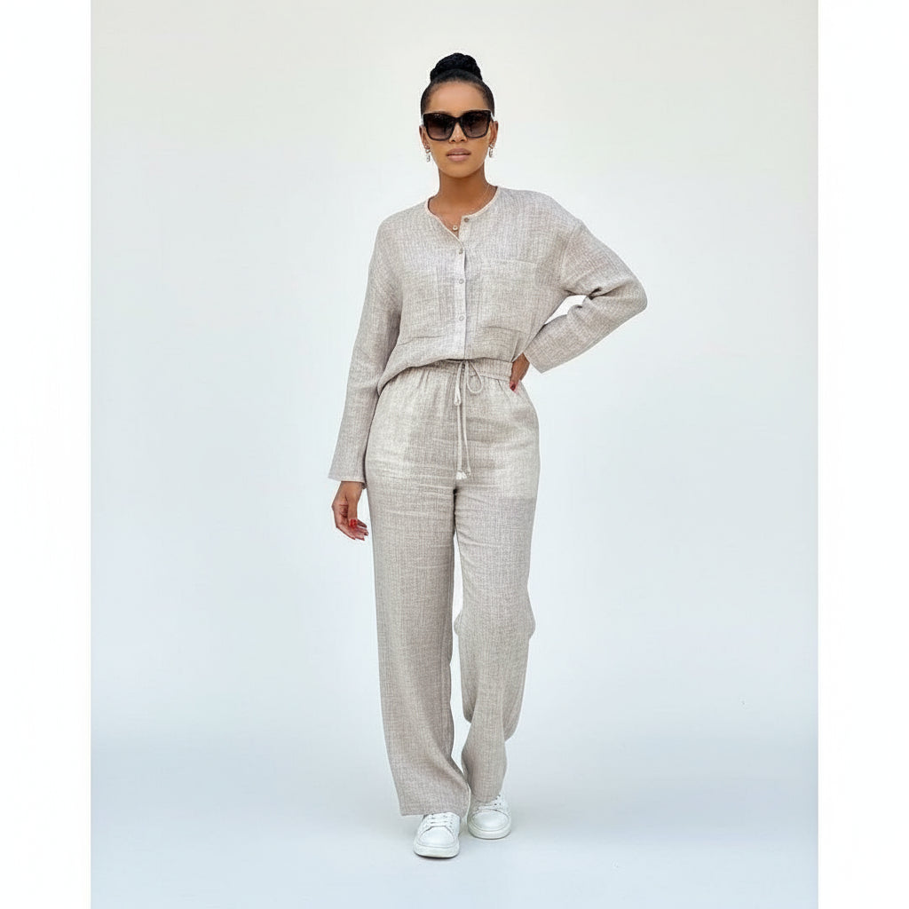 A person standing beside a red suitcase, wearing a beige 2 piece lounge set with a Chinese collar.