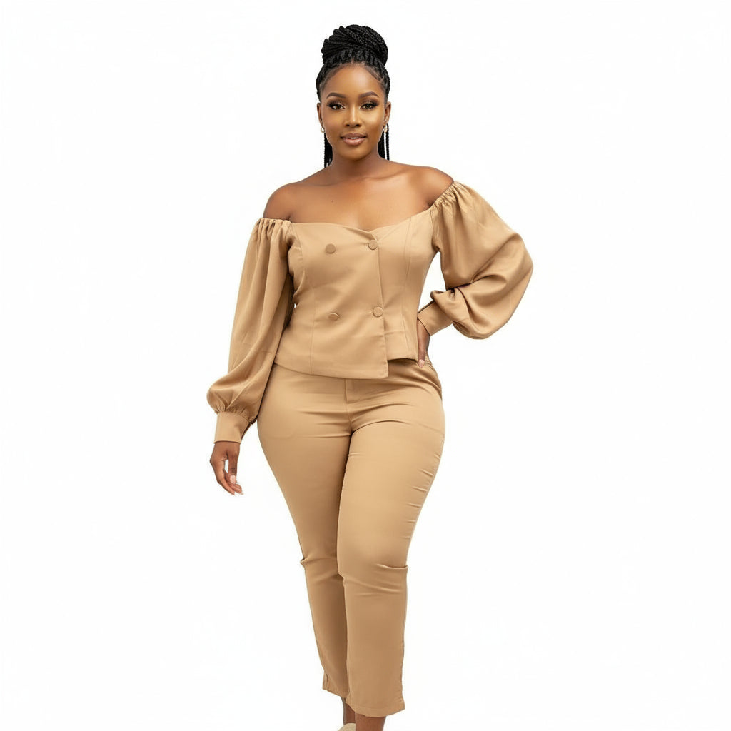 A person wearing an off-shoulder formal suit in beige, consisting of a top with puffed sleeves and a matching trouser, standing against a marble background.