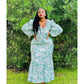 A woman standing outdoors wearing a green floral maxi dress with a V-neck and puff sleeves.