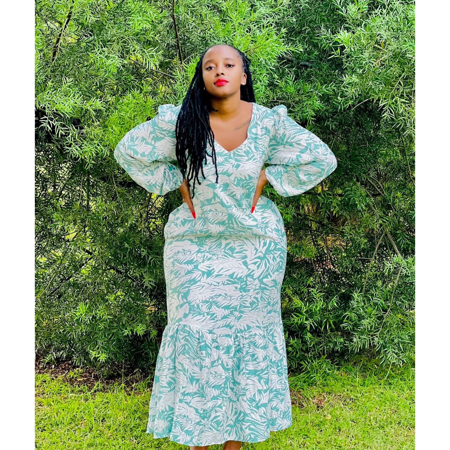 A woman standing outdoors wearing a green floral maxi dress with a V-neck and puff sleeves.