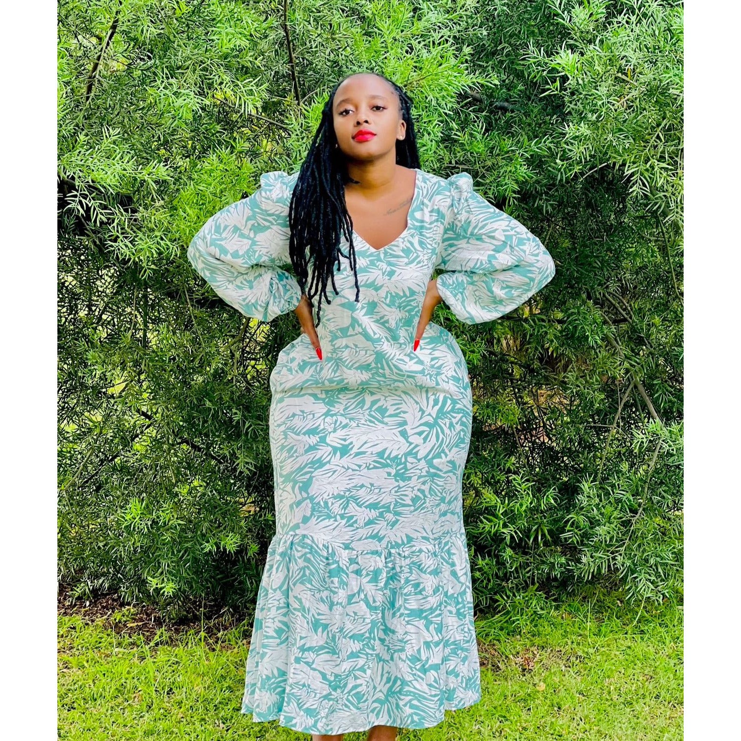 A woman standing outdoors wearing a green floral maxi dress with a V-neck and puff sleeves.