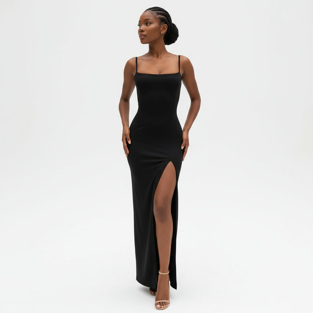 A woman modeling a black backless split dress with spaghetti straps and a high slit.