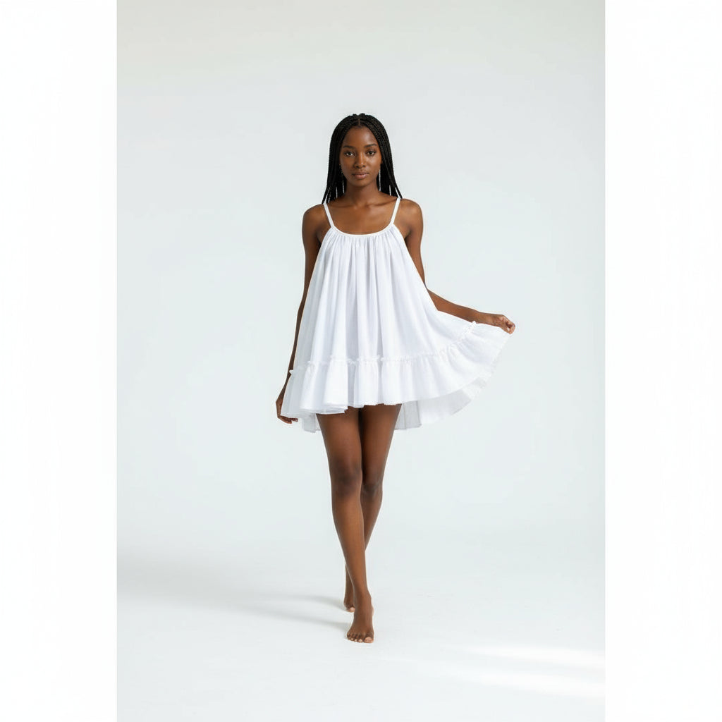 A woman standing on a pathway wearing a white sleeveless open back mini dress.